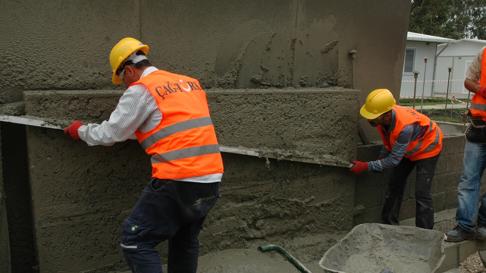 Construction workers in hard hats and high visibility vests plastering a wall in full sun