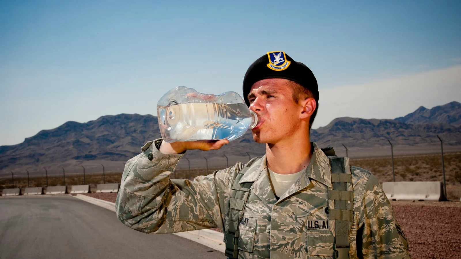 A worker on duty drinks from a water bottle in desert heat